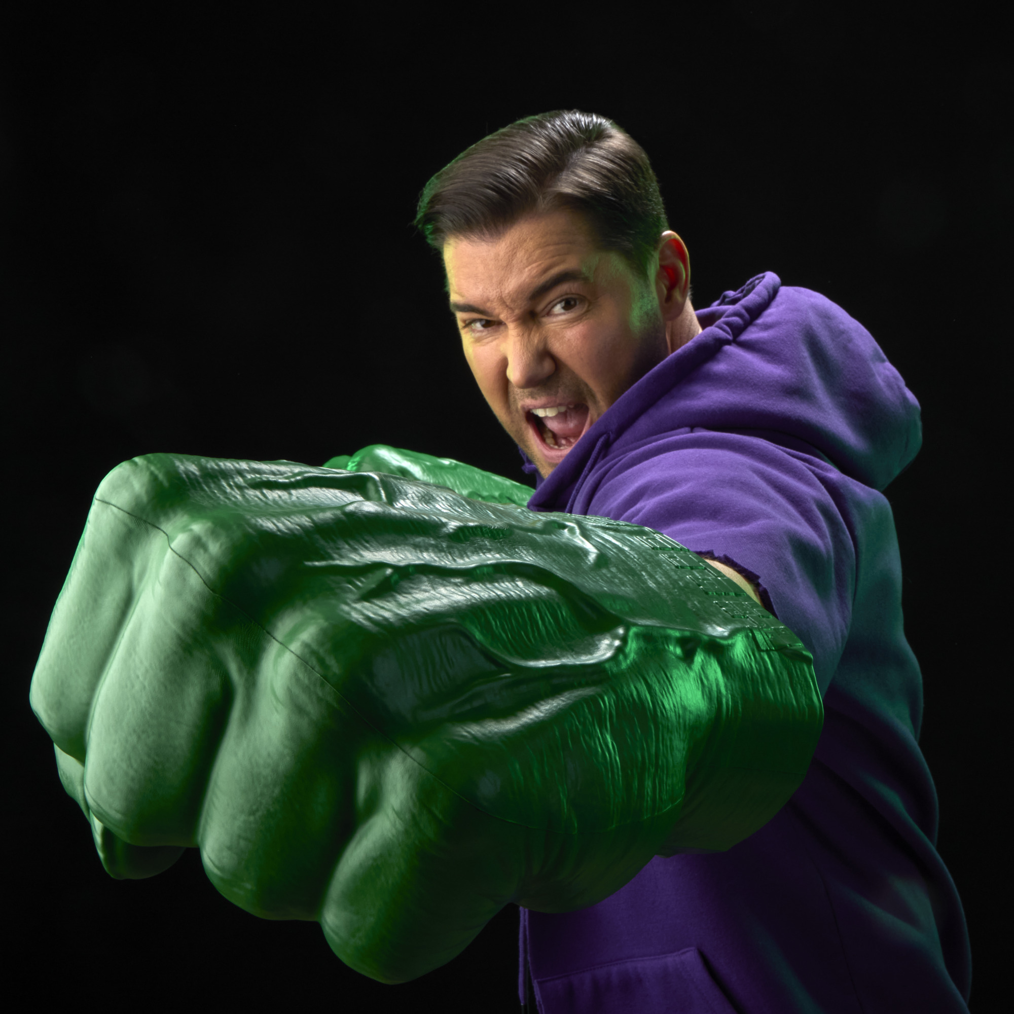 A roaring man with two Hulk Fists pretends to punch with them against a black background