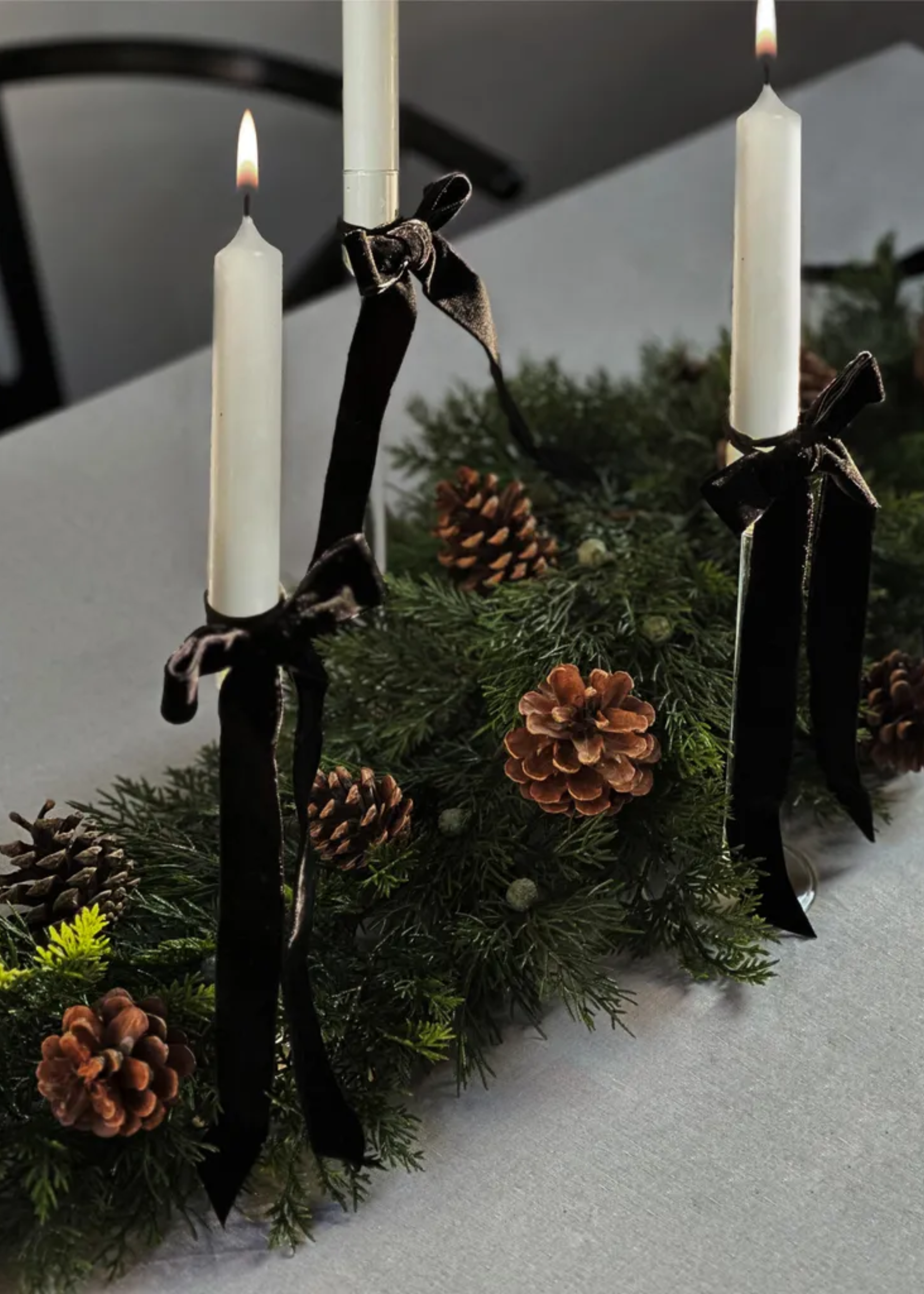 A table with a pinecone garland and lit tapers with black velvet ribbon bows