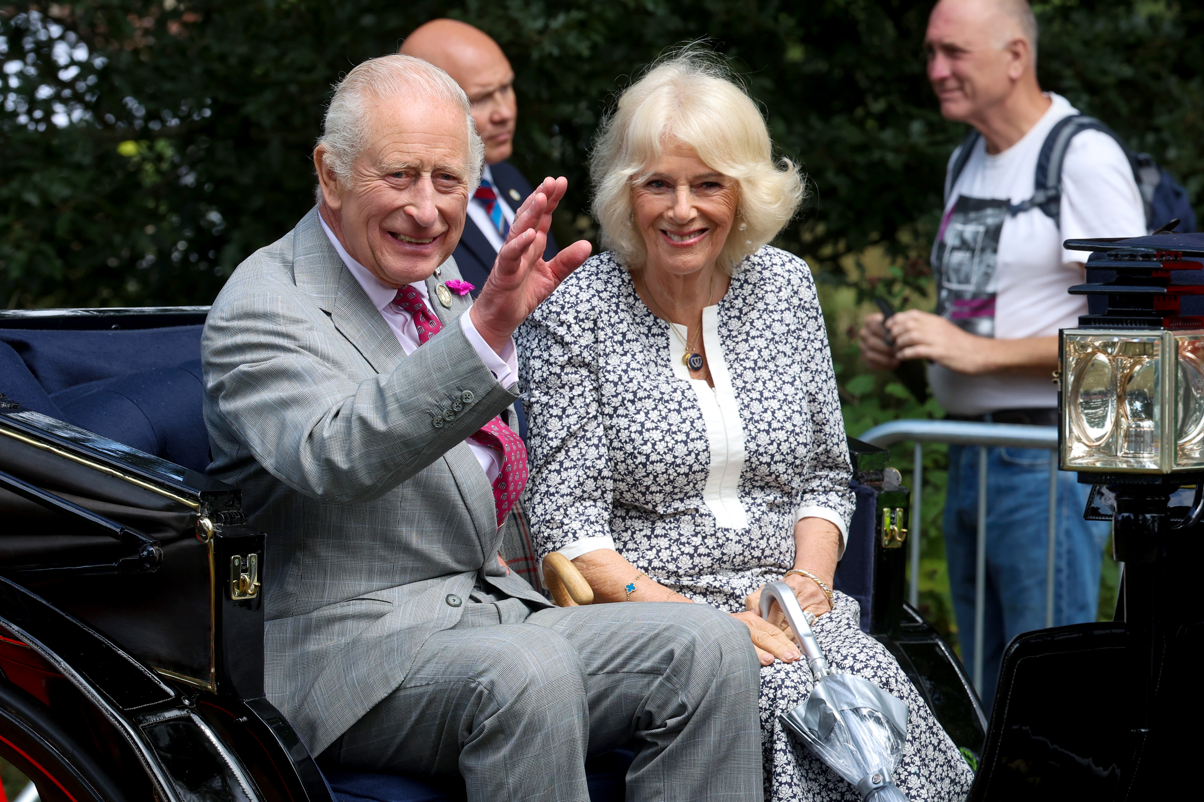 Queen Camilla and King Charles riding in a carriage waving and smiling