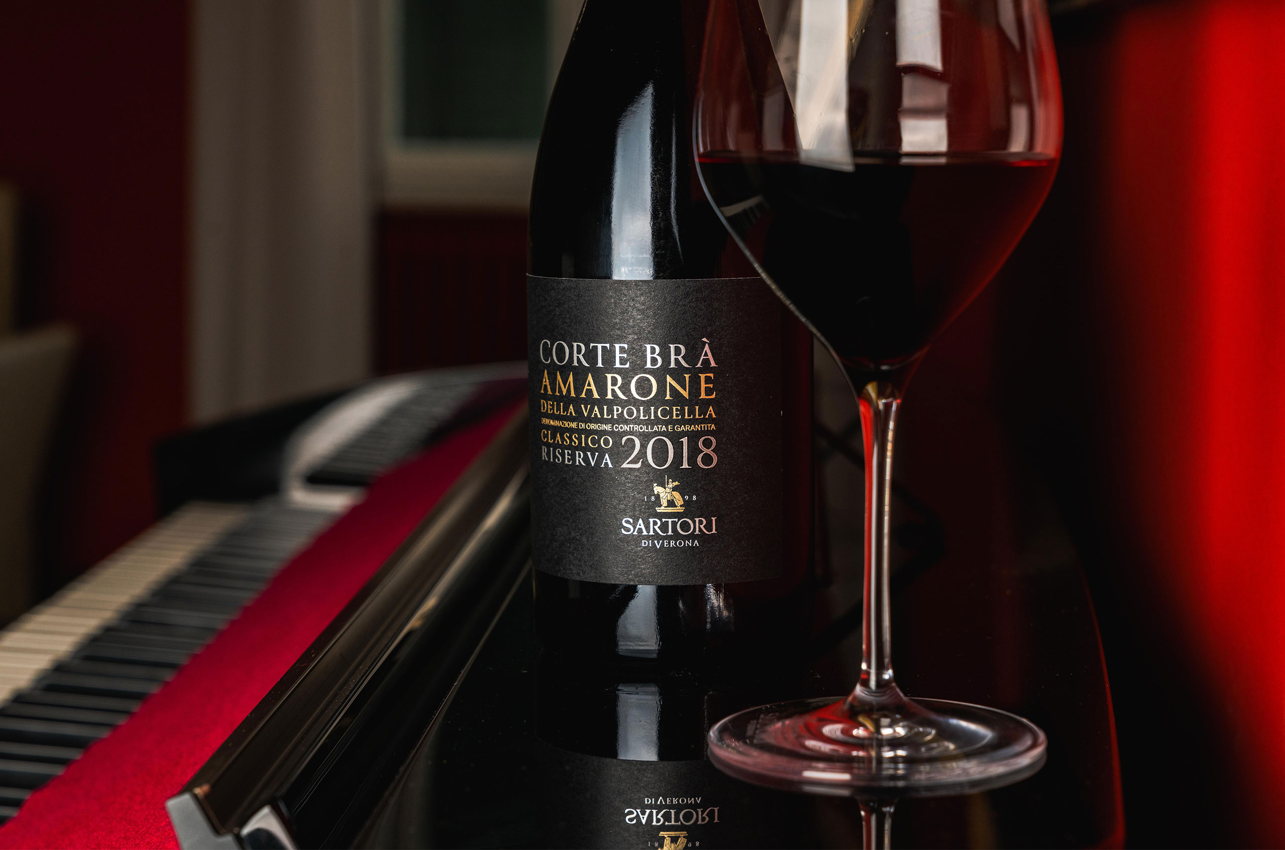 Image of bottle of red wine next to a piano.