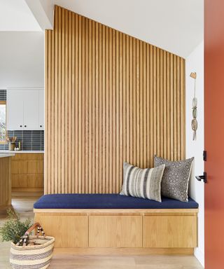 A boot bench area with wall clad in white oak slats, and a blue fabric-upholstered built-in bench with storage