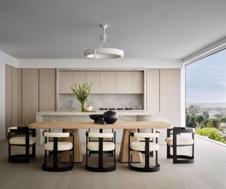 A neutral dining room with a floor to ceiling window and modern dining chairs