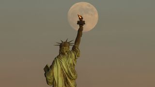A nearly full moon rises above the Statue of Liberty on June 23, 2021.