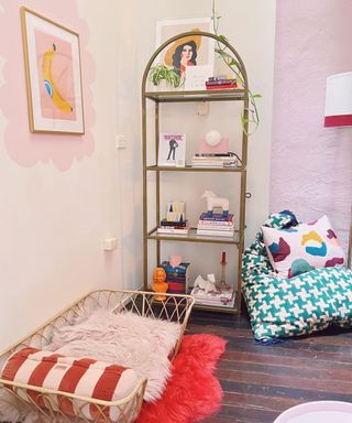 A pink room with a wooden arched shelf, a blue houndstooth chair, and a woven pet bed