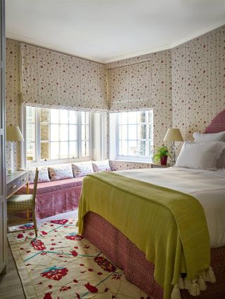 floral wallpaper with the same fabric on blinds, green and pink color scheme, rug, dressing table, window seat