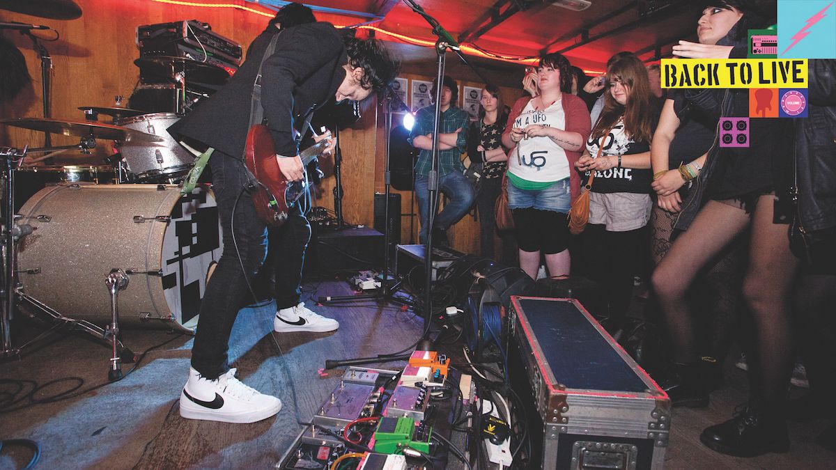 Man rocks out on stage with his band and a huge pedalboard