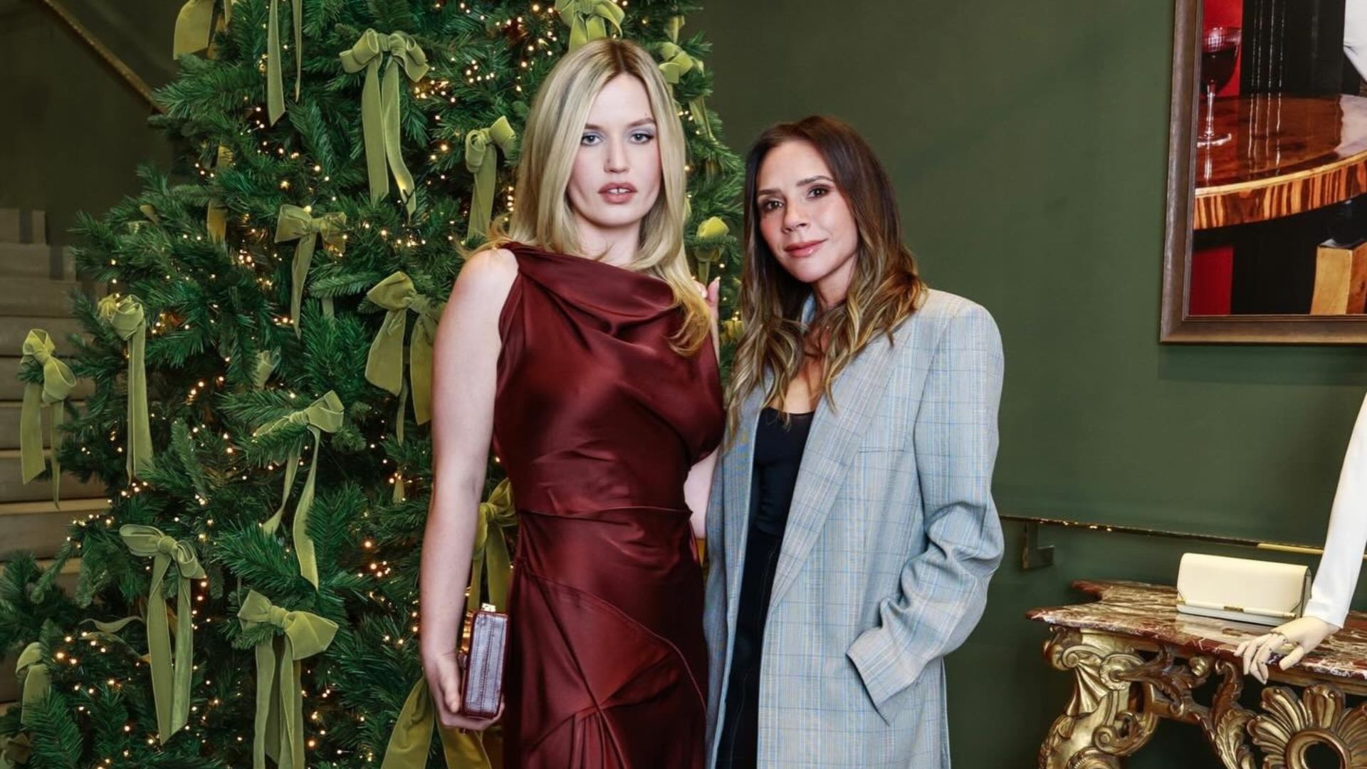 Victoria Beckham poses for a photo in front of a Christmas tree with Georgia May Jagger wearing a grey blazer with a black leather pencil skirt and brown peep-toe heels.