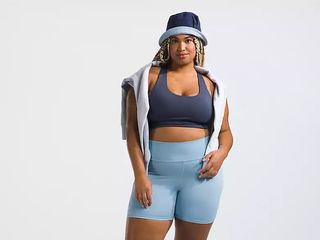model wears blue bike short and dark blue bra with sweater over the shoulders and a bucket hat.