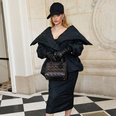 Rihanna wearing a black peplum style coat with a black cap 