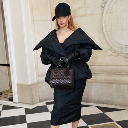 Rihanna wearing a black peplum style coat with a black cap 