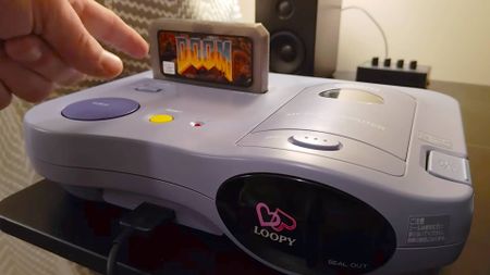 Hand pointing at custom DOOM cartridge inserted into Casio Loopy console.