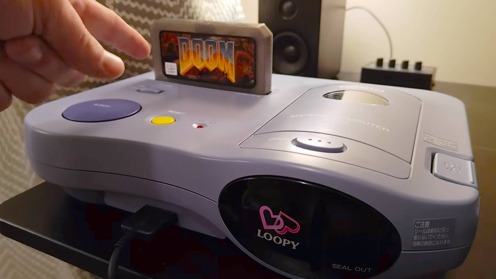 Hand pointing at custom DOOM cartridge inserted into Casio Loopy console.