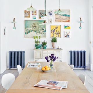 Blue painted radiators in dining room of large home with gallery wall and large wooden dining table
