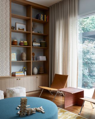 a living room with open shelving with light blue wall color, a light blue ottoman sits in the middle surrounded by chairs