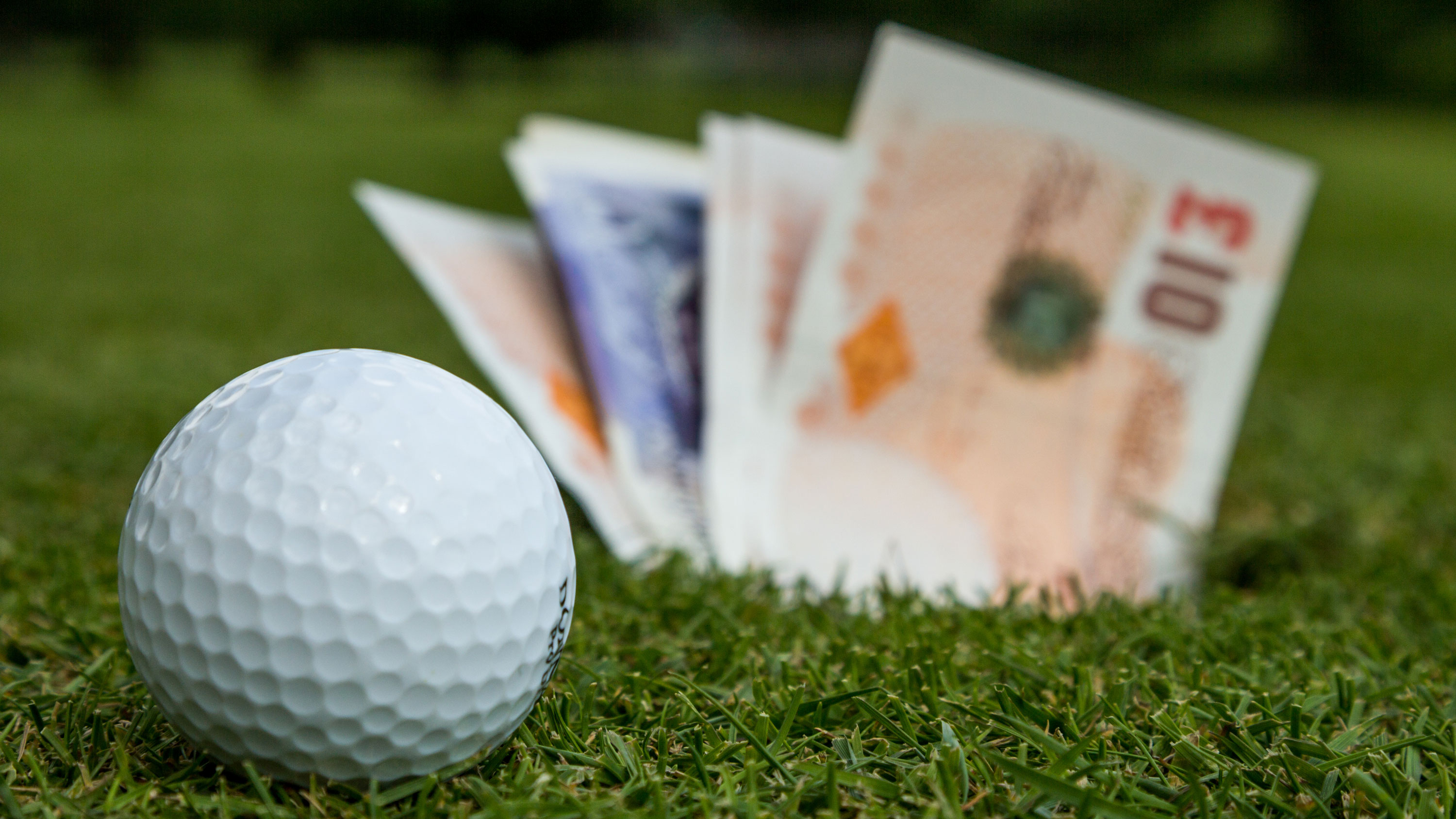 a golf ball in front of a fan of English money denoting golf being too expensive and golfers being taken advantage of