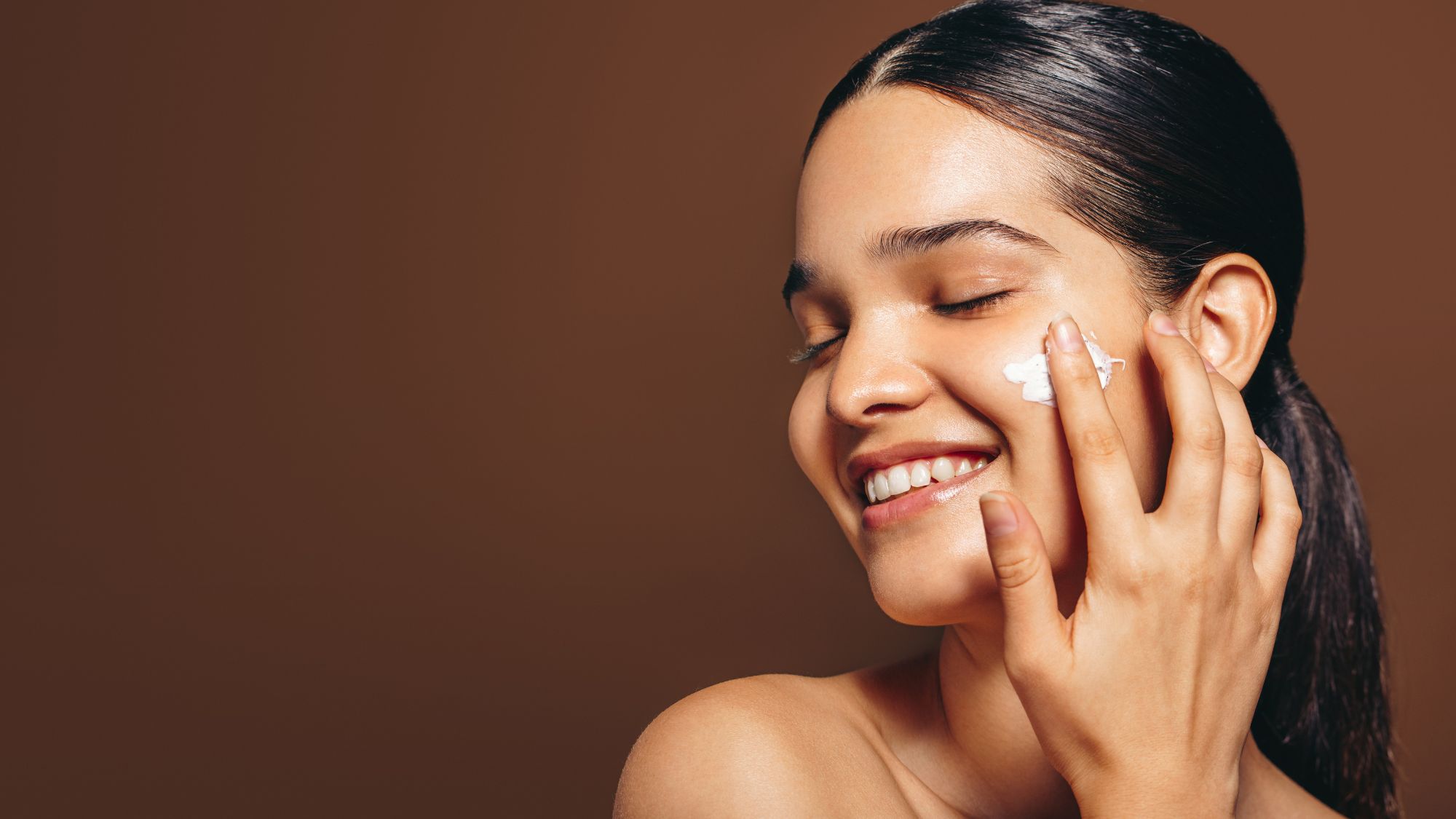 Woman applying cream to her face with eyes closed