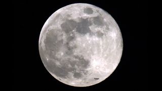 an airplane flies in front of the full moon in a dark sky