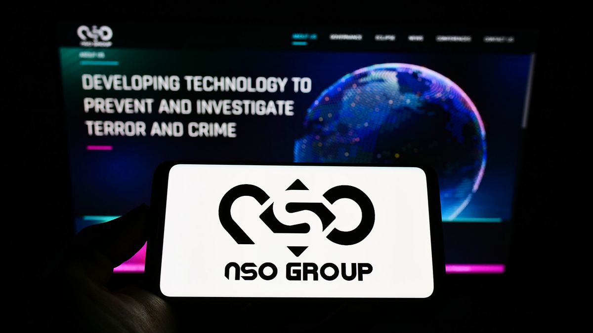 Person holding mobile phone with logo of technology company NSO Group Technologies Ltd. on screen in front of web page