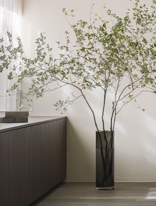 A tall vase with green branches by a window in the Karimoku Case Study house