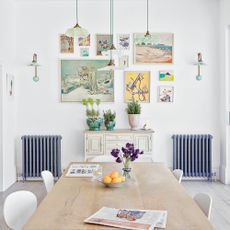 White kitchen dining room with gallery wall, pendant lights, dining table and blue cast iron radiators