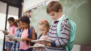 Elementary school children stand in front of blackboard using iPad tablet computers