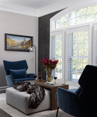 Arched window with shutters, two facing blue armchairs and coffee table