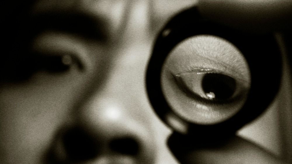 black and white photo of a man&#039;s eye as he looks through a small glass lens that appears to have flipped his eye upside down