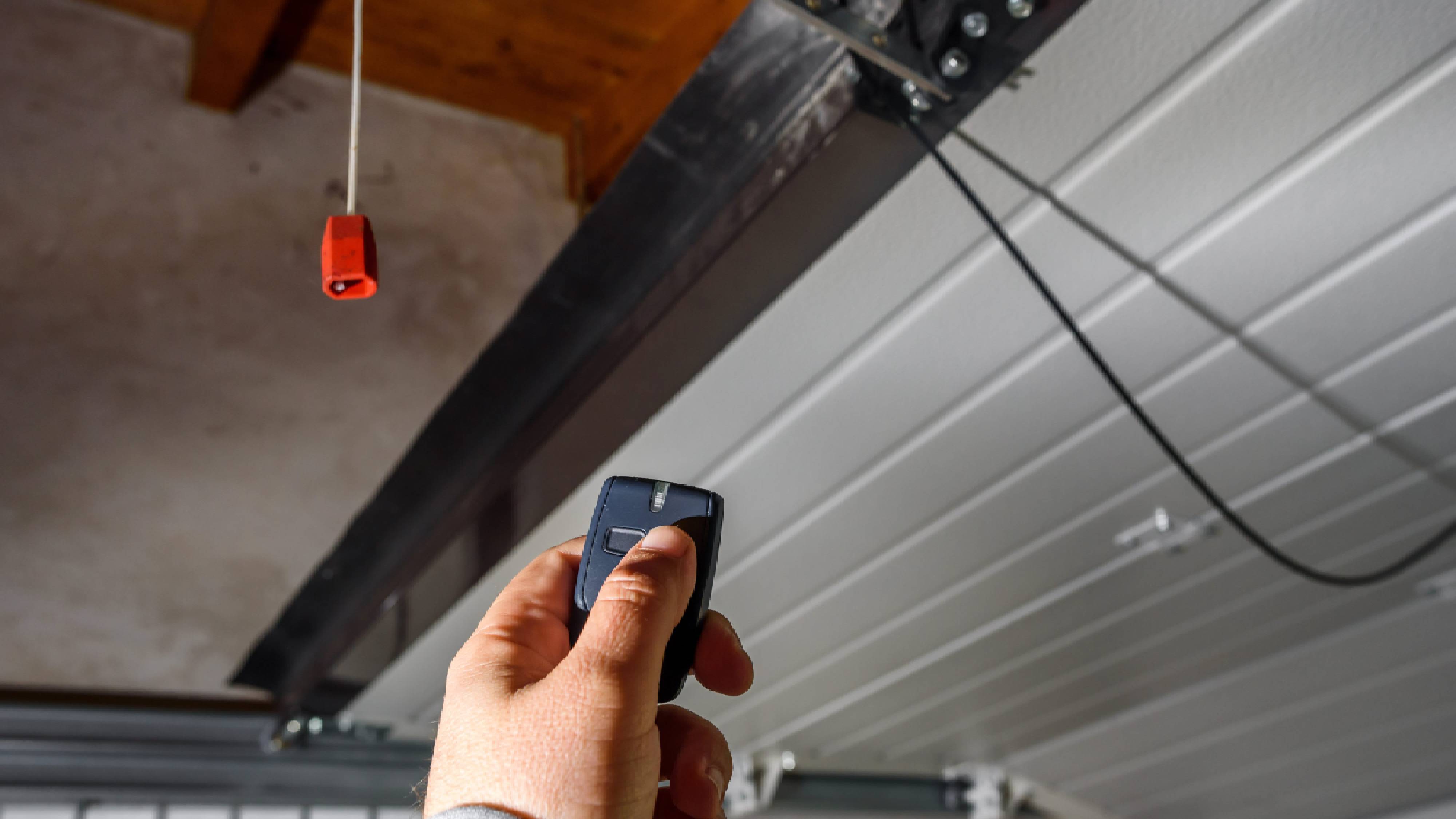 Hand pointing a garage remote up toward the ceiling motor unit during the pairing process