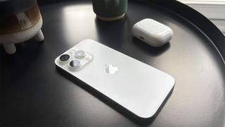 Apple iPhone 16 Pro smartphone face down on shiny black surface next to AirPods case