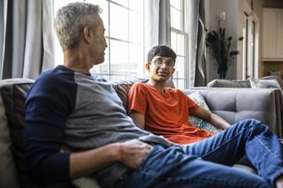 Father and teen son talking while sitting on the sofa together at home