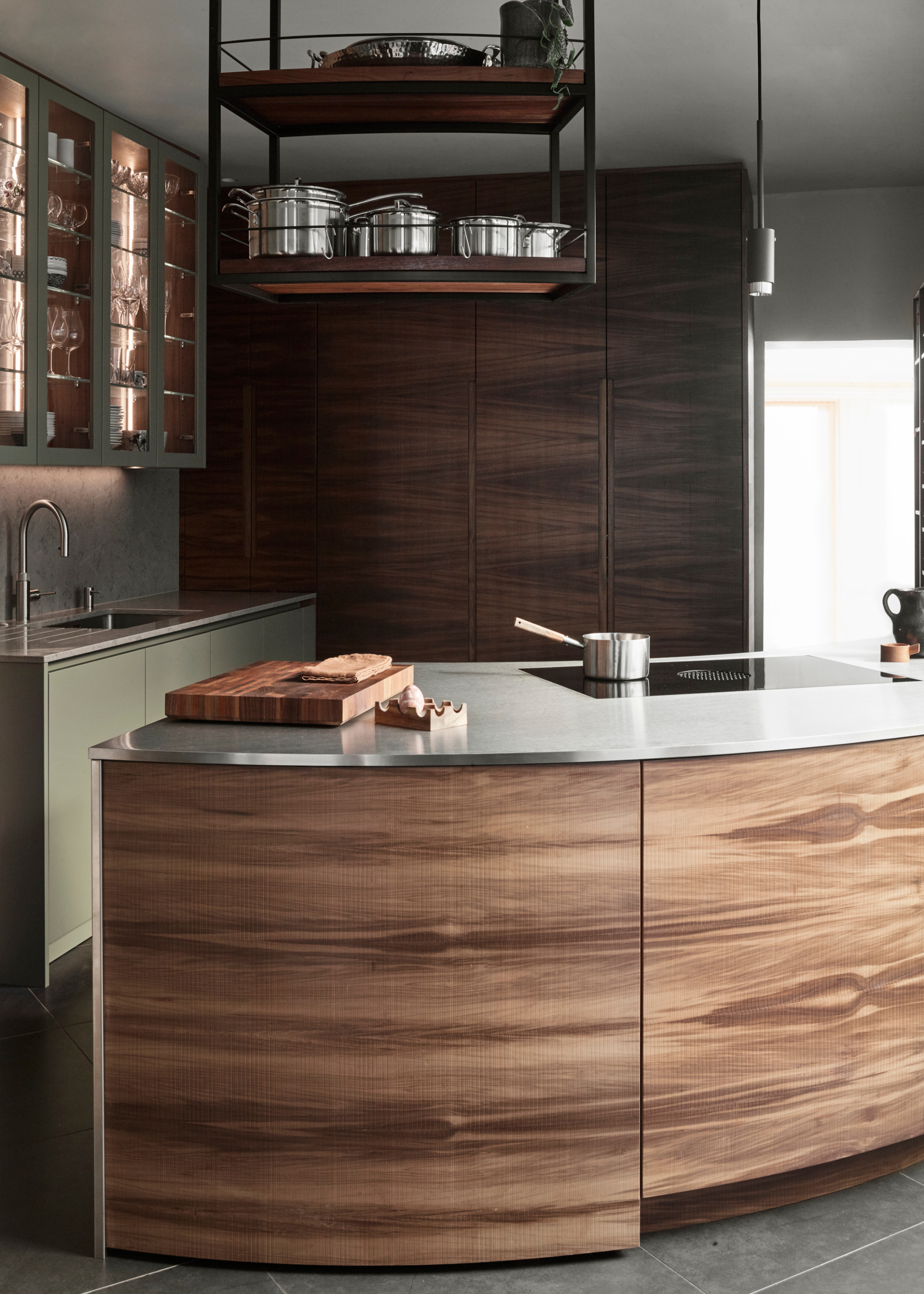 a modern wooden kitchen with a curved island and sage green cabinetry