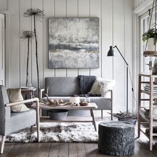 White living room with white wall cladding grey upholstered sofa abstract grey artwork and plush grey rug, with grey scandi sofas and wooden coffee table