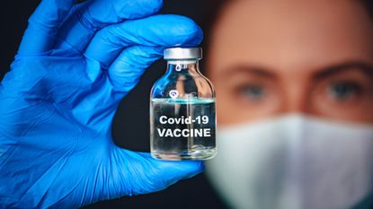A woman wearing mask and gloves holds a vial of Coronavirus vaccine.