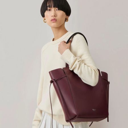 woman wears cream knit sweater and burgundy tote bag