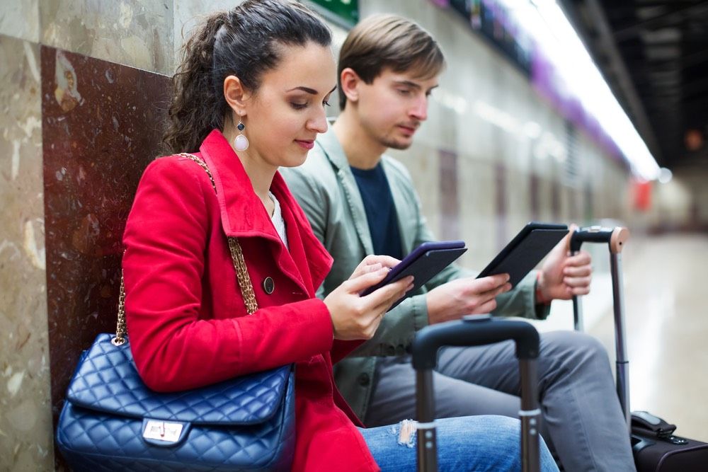 Subway passengers reading with modern gadgets as waiting a train.