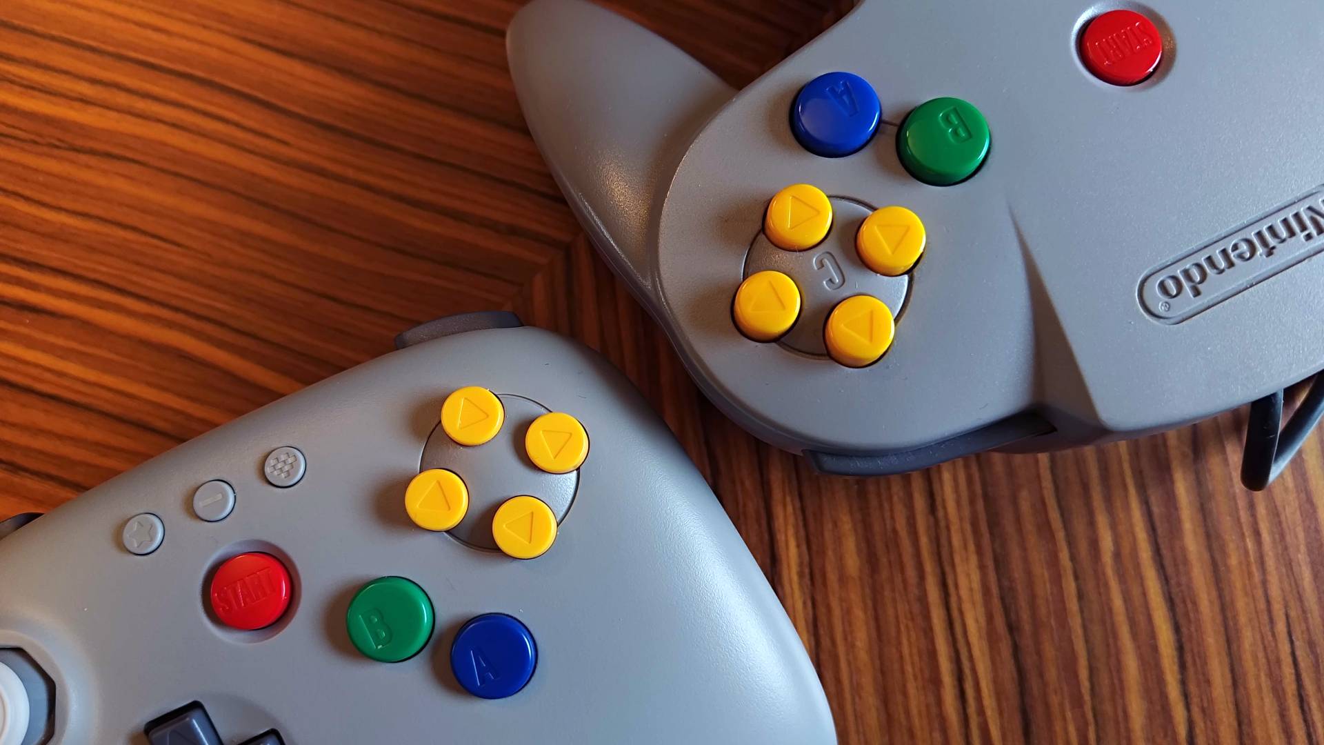 Close up of 8Bitdo n64 controller and original controller buttons side by side on woodgrain table.