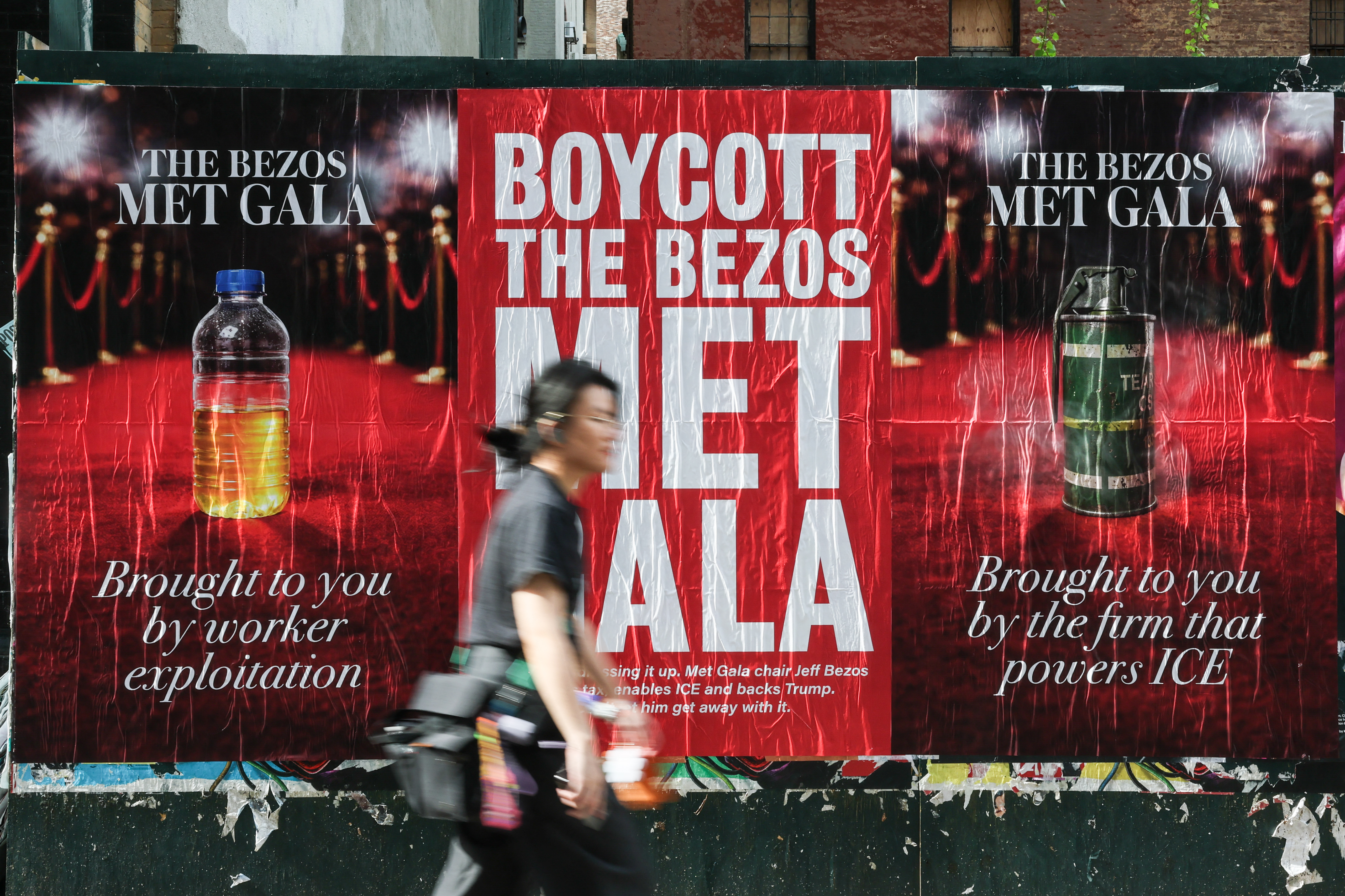 a person walking past posters calling for a boycott of the 2026 met gala