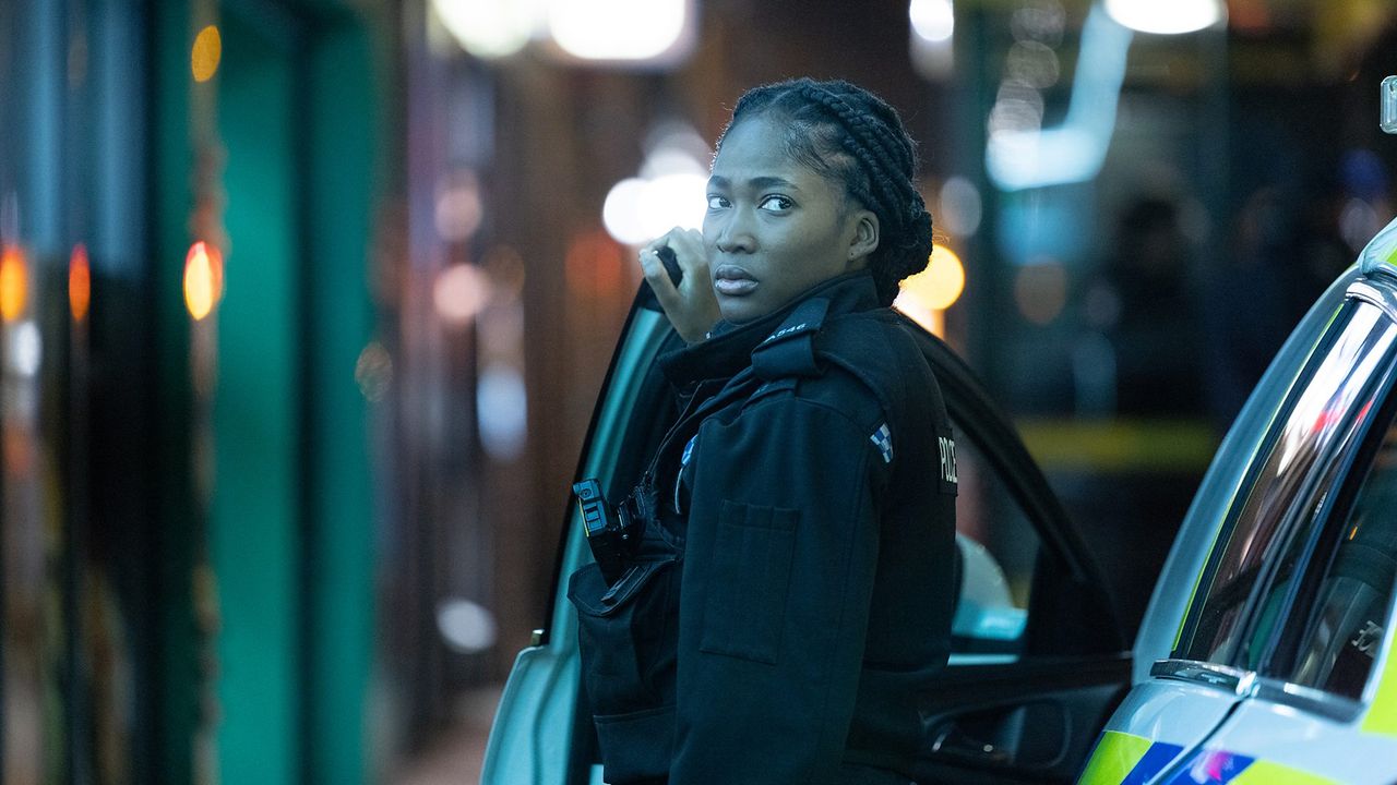 Adelayo Adedayo as Rachel, standing next to a police car.