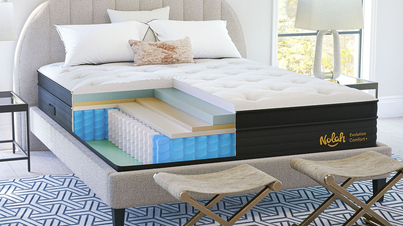 The Nolah Evolution Comfort+ mattress on a bed frame in a bedroom, a cross section at the corner shows the interior foam and spring layers of the hybrid mattress.