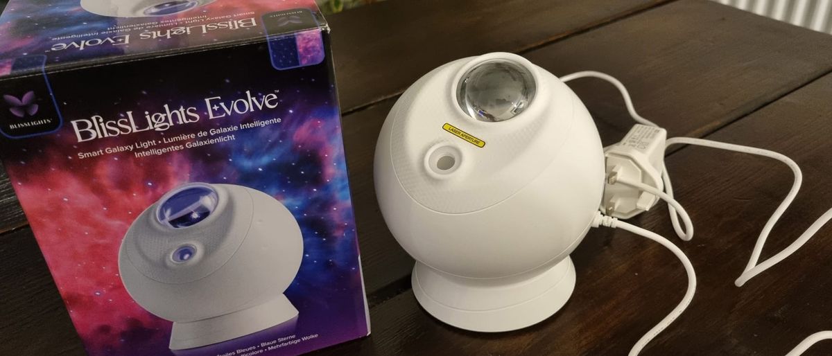 The BlissLights Sky Lite Evolve on a table next to it&#039;s packaging and power cable