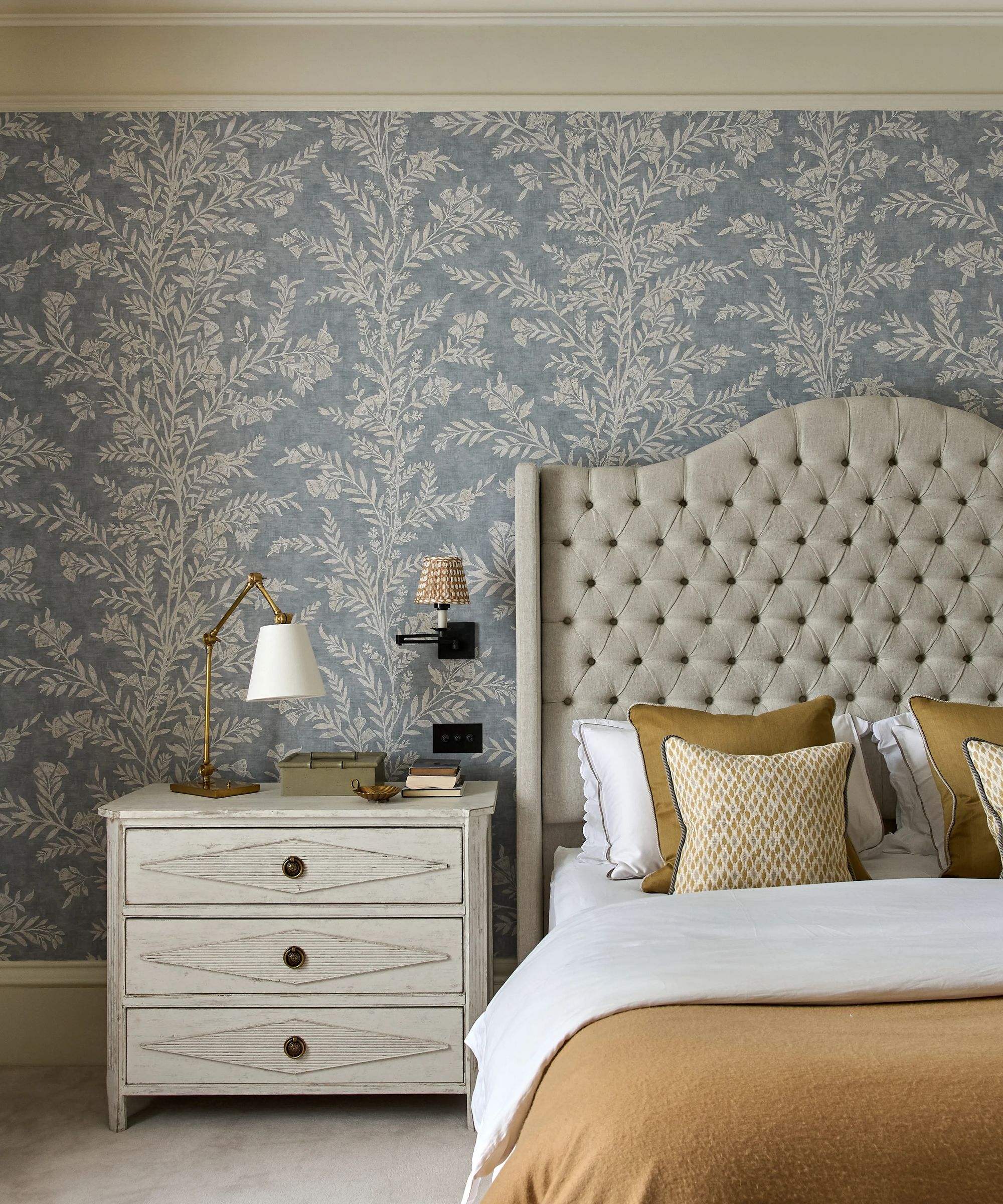 Bedroom with floral blue living room and gray button back headboard with pale orange and white bedding