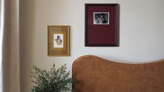 Close-up image of a white wall over a burnt orange headboard. There is a small yellow frame next to a burgundy frame