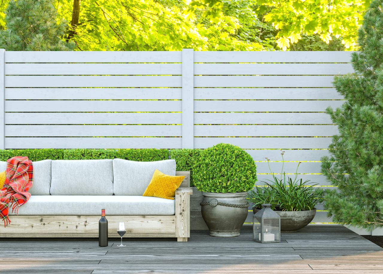 Garden decking with a wine bottle and glass set in front of a row of seating and plants