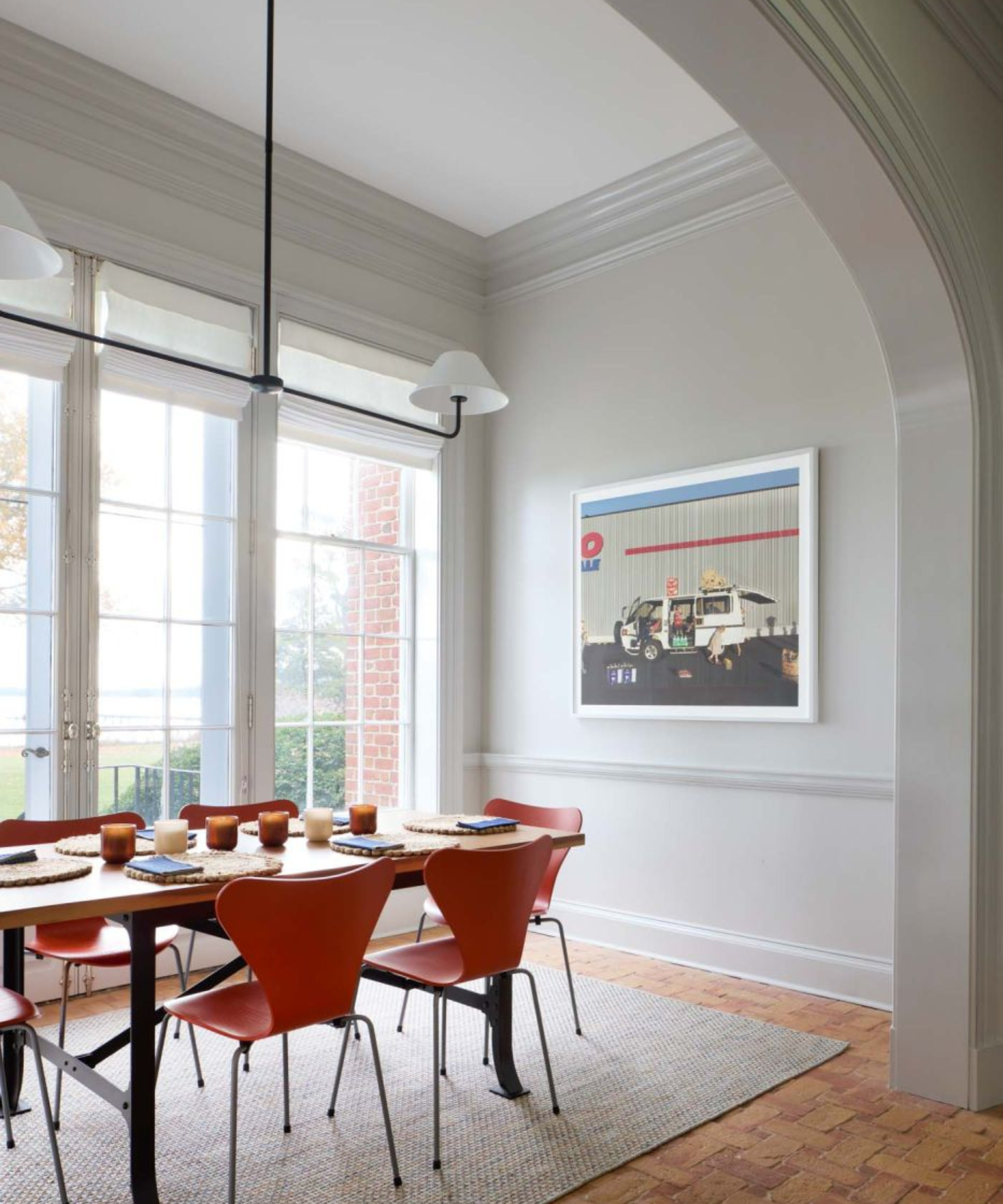A bright dining room with greige walls, an arched entryway, sliding glass doors and orange chairs