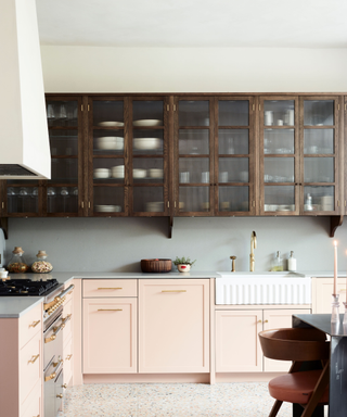 A kitchen with pink bottom cabinets and wooden top cabinets with glass fronts