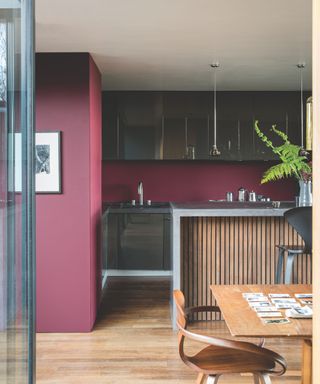 A kitchen with a wood kitchen island, burgundy walls, and glass cabinetry