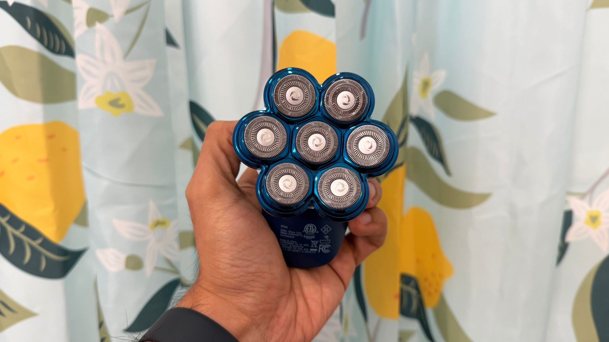 Dollar Shave Club Head Shaver held in hand in front of shower curtain