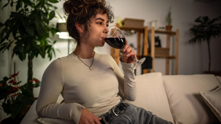 A woman sat on her sofa in the evening drinking a glass of red wine