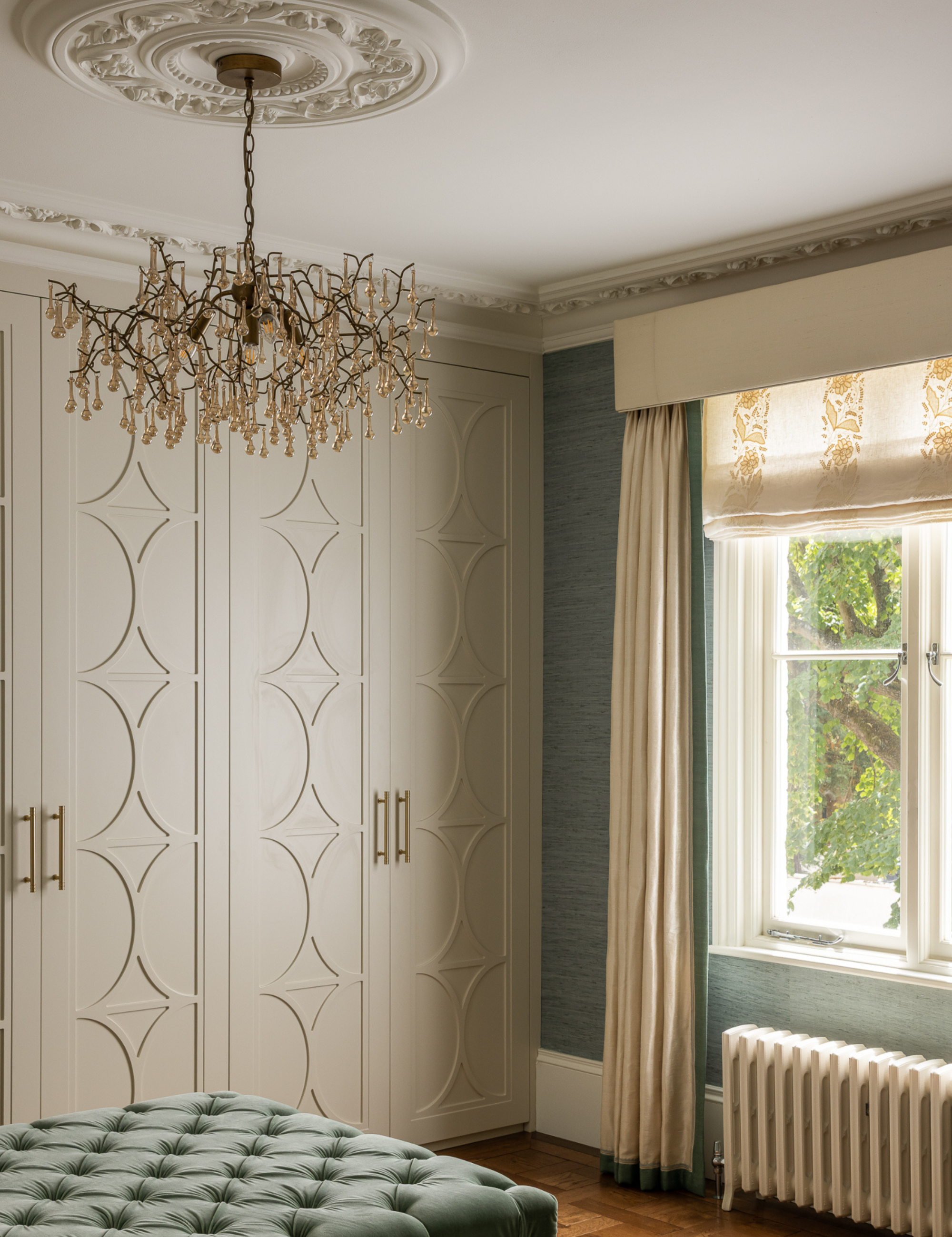 Ornate dressing room featuring a crystal chandelier, sky blue tufted ottoman, and layered window treatments
