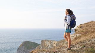 Woman wearing a backpack with long straps hiking by the coast